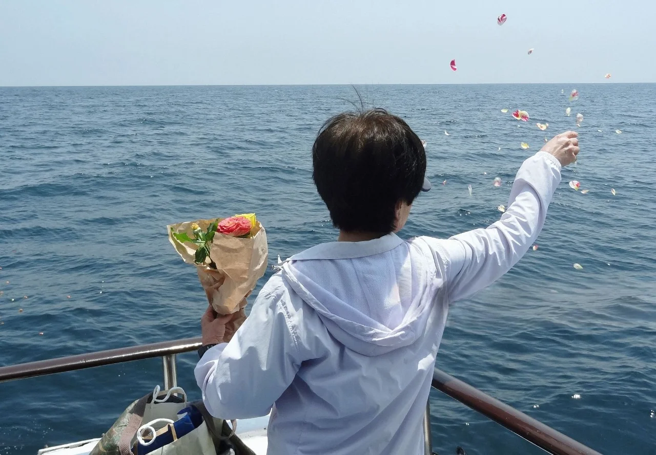 Person scattering flower petals at sea during memorial
