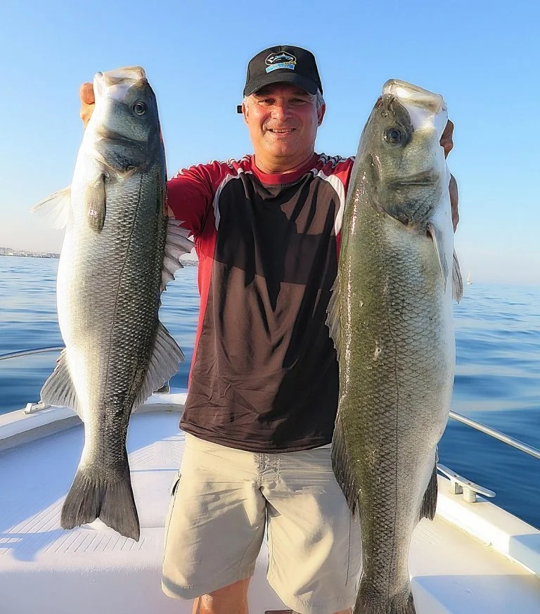 Man holding two large bass fish caught on fishing charter